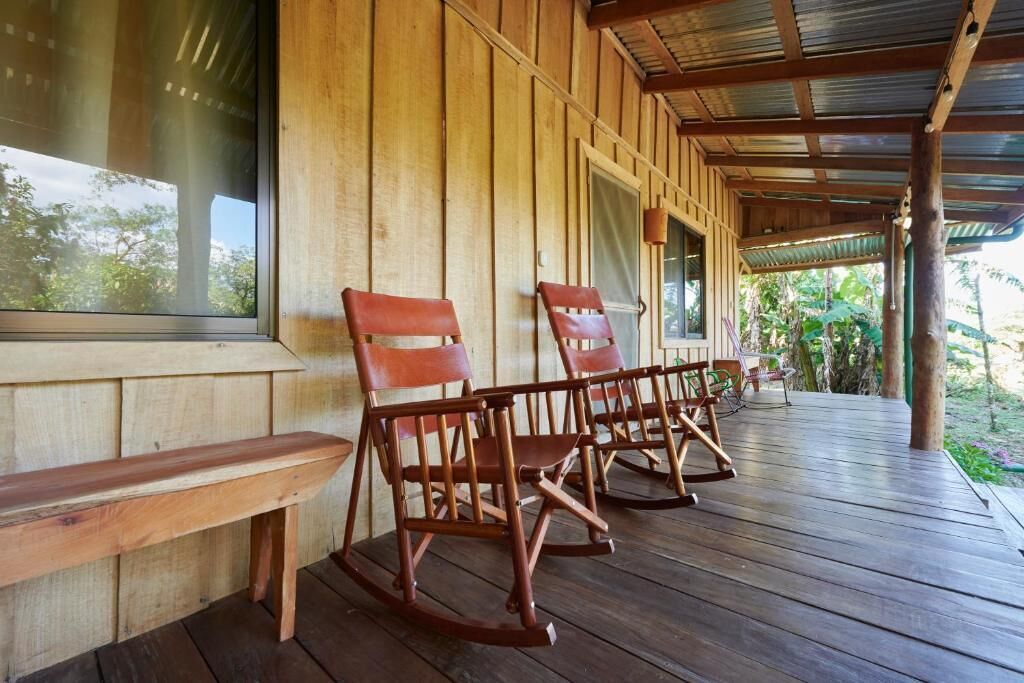 Un porche de madera con mecedoras y un banco, con vista a un jardín.