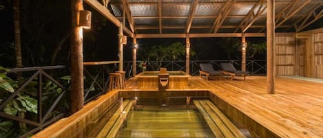 A wooden deck with a pool, surrounded by bamboo structures and metal railings.