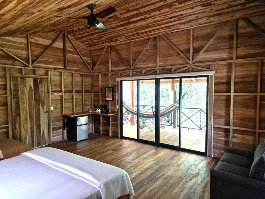 A wooden cabin with a bed, a small kitchenette, and a hammock outside.