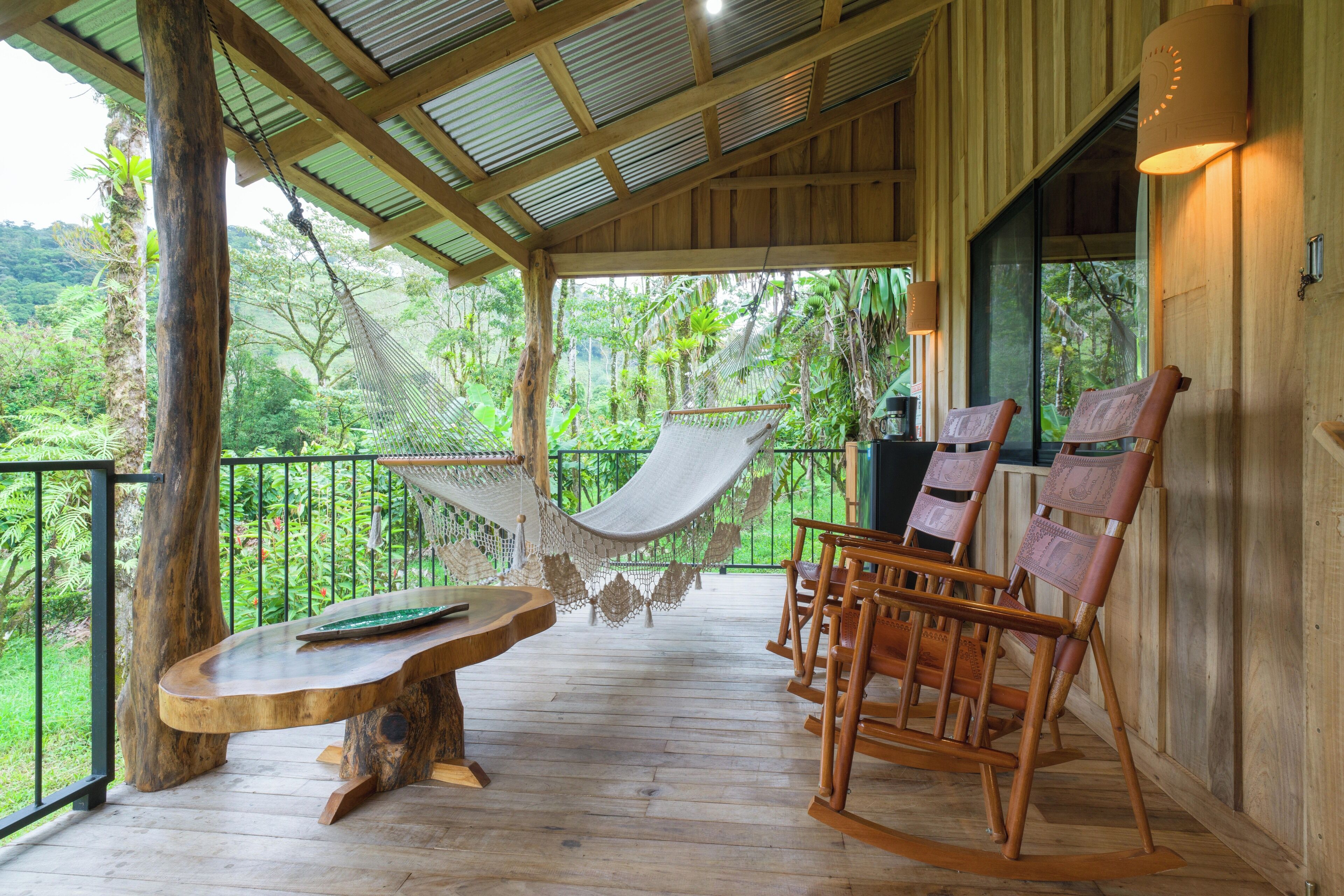 A wooden deck with a hammock, wooden chairs, and a table.
