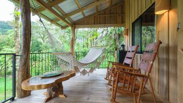 A wooden deck with a hammock, wooden chairs, and a table.