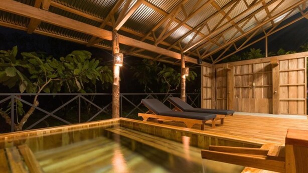 An outdoor swimming pool with wooden deck and lounge chairs, surrounded by a wooden fence and tropical foliage. - Finca Amistad Cacao Lodge (Bijagua)