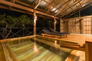 An outdoor swimming pool with wooden deck and lounge chairs, surrounded by a wooden fence and tropical foliage. - Finca Amistad Cacao Lodge (Bijagua)