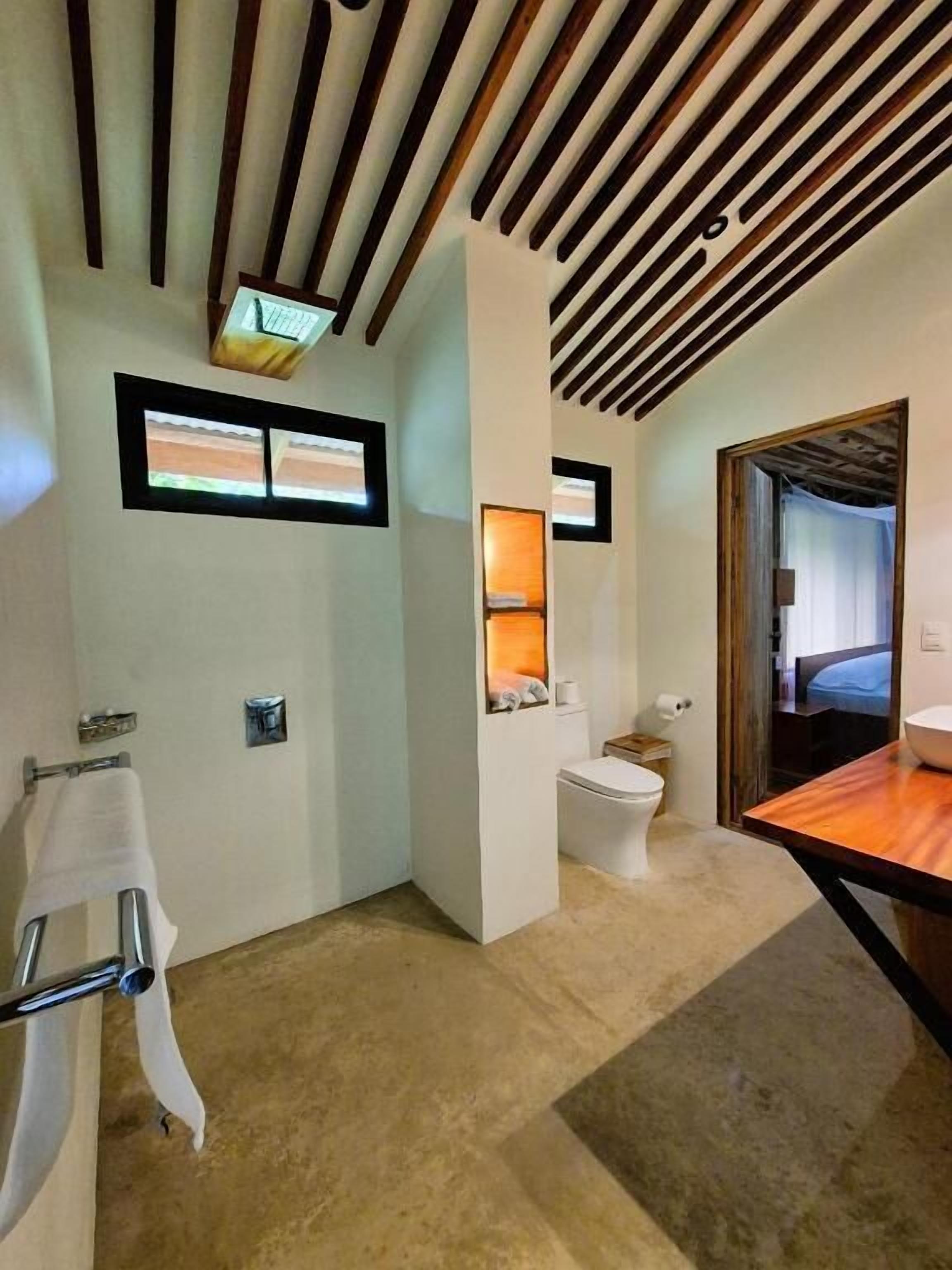 A modern bathroom with a wooden ceiling, a toilet, a sink, and a towel rack.
