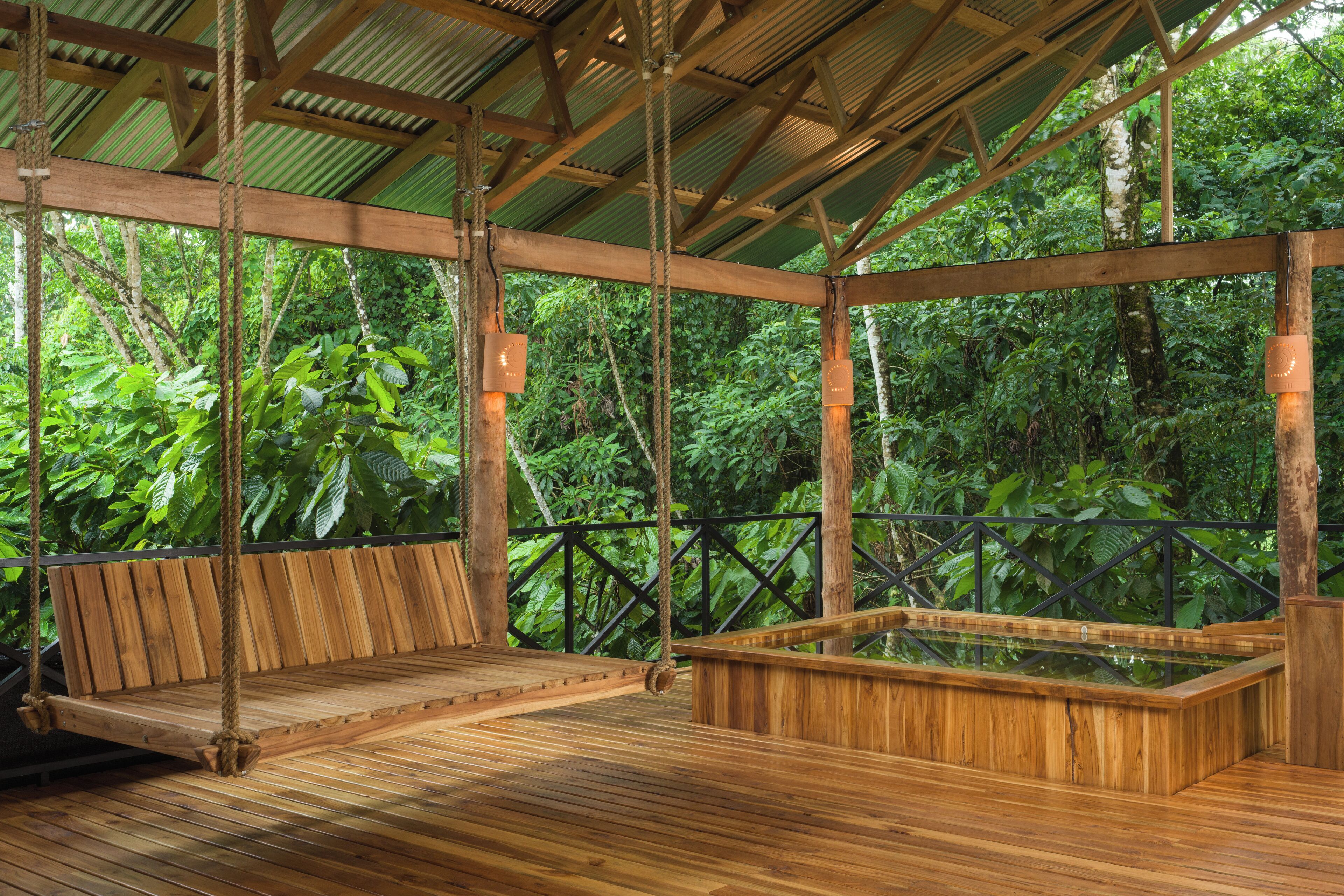 A wooden deck with a swing, surrounded by lush greenery.