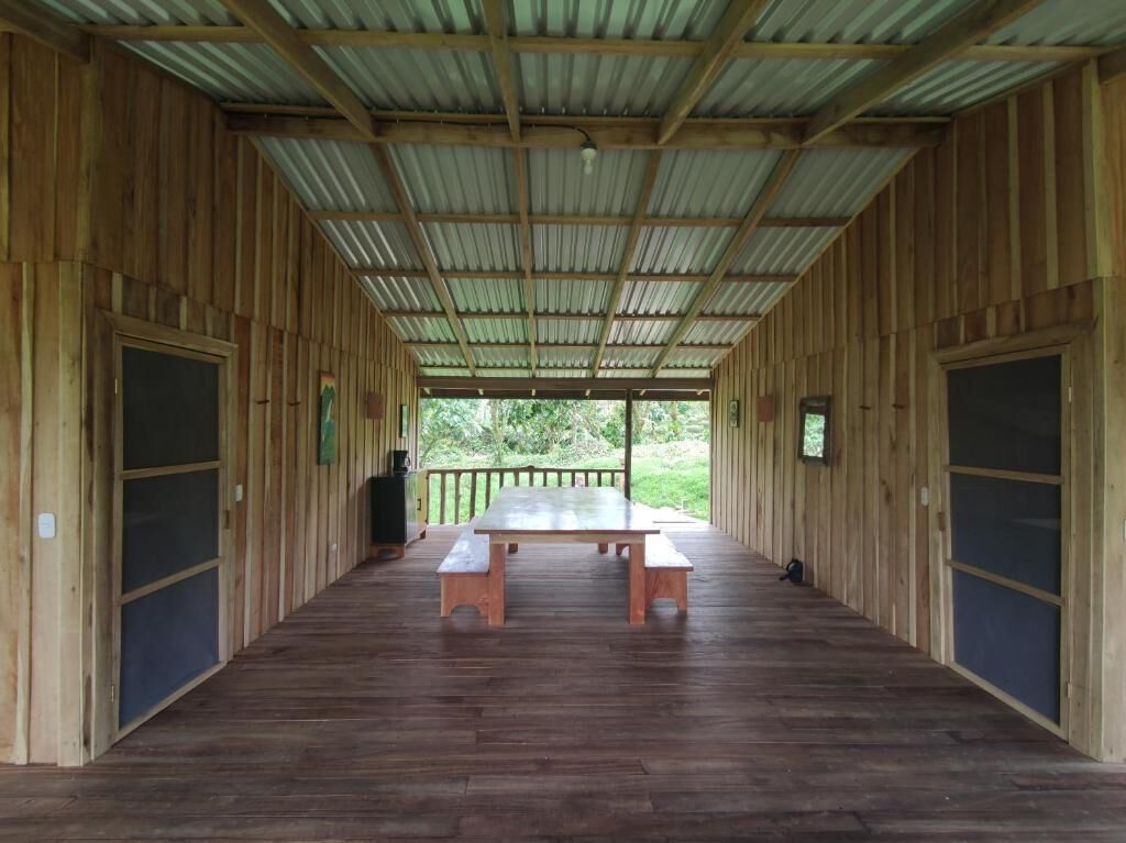 A covered wooden structure with a central table and benches, surrounded by wooden walls and doors.