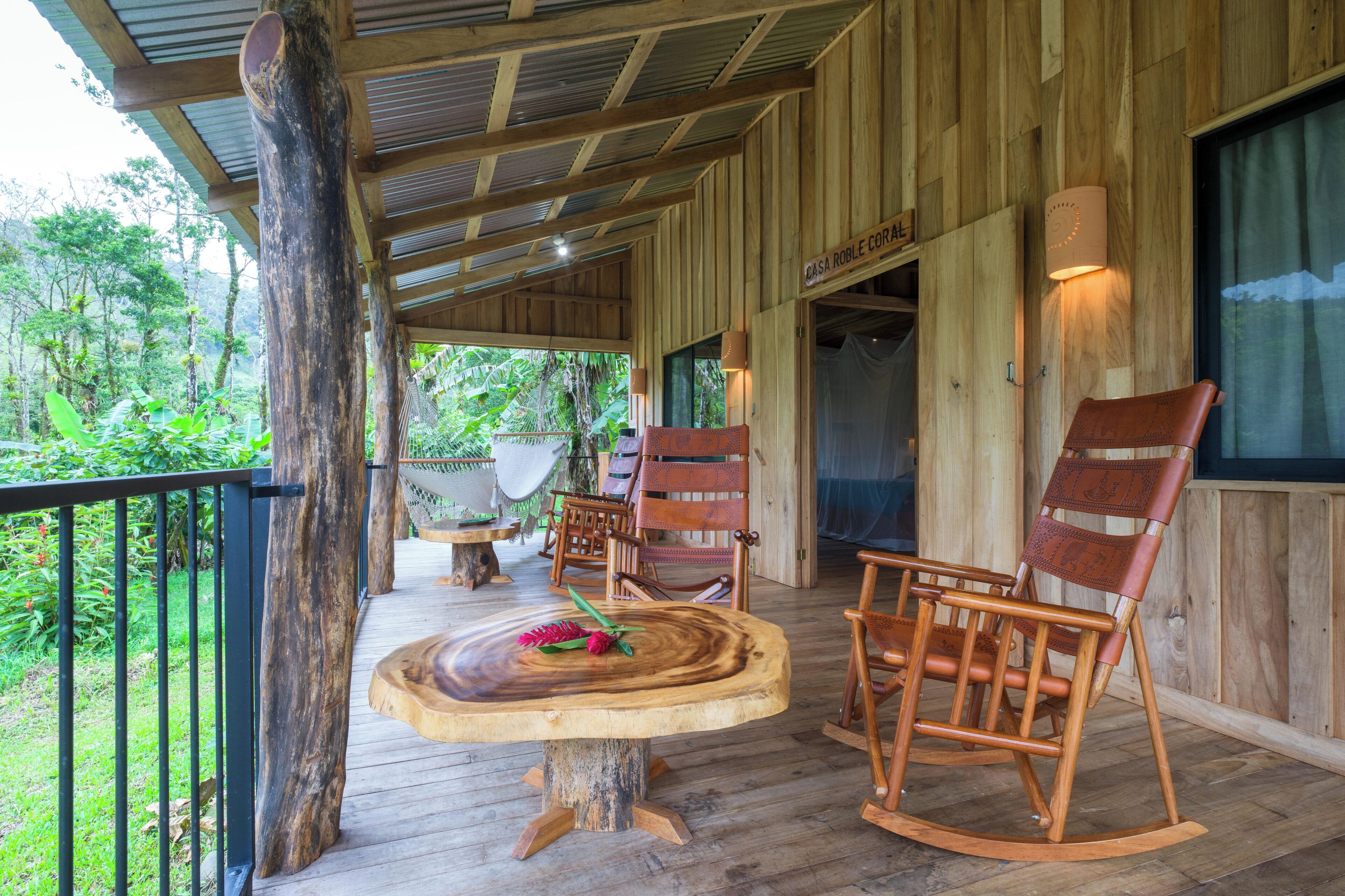 A wooden deck with a round table and two rocking chairs, surrounded by wooden walls and a railing.