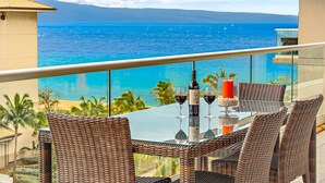 A balcony with wicker furniture, a glass table, and two wine glasses with a bottle of wine. - Maui Resort Rentals: Honua Kai - 3 Total Bedrooms, 6th Floor Partial Ocean AND West Maui Mountain Views! (Lahaina)