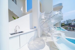 Une cuisine moderne dotée d’un évier et de placards, un espace piscine avec un toboggan, et une vue dégagée sur les bâtiments environnants.