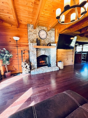 A cozy living room with a stone fireplace, wooden walls, a clock, and a TV.