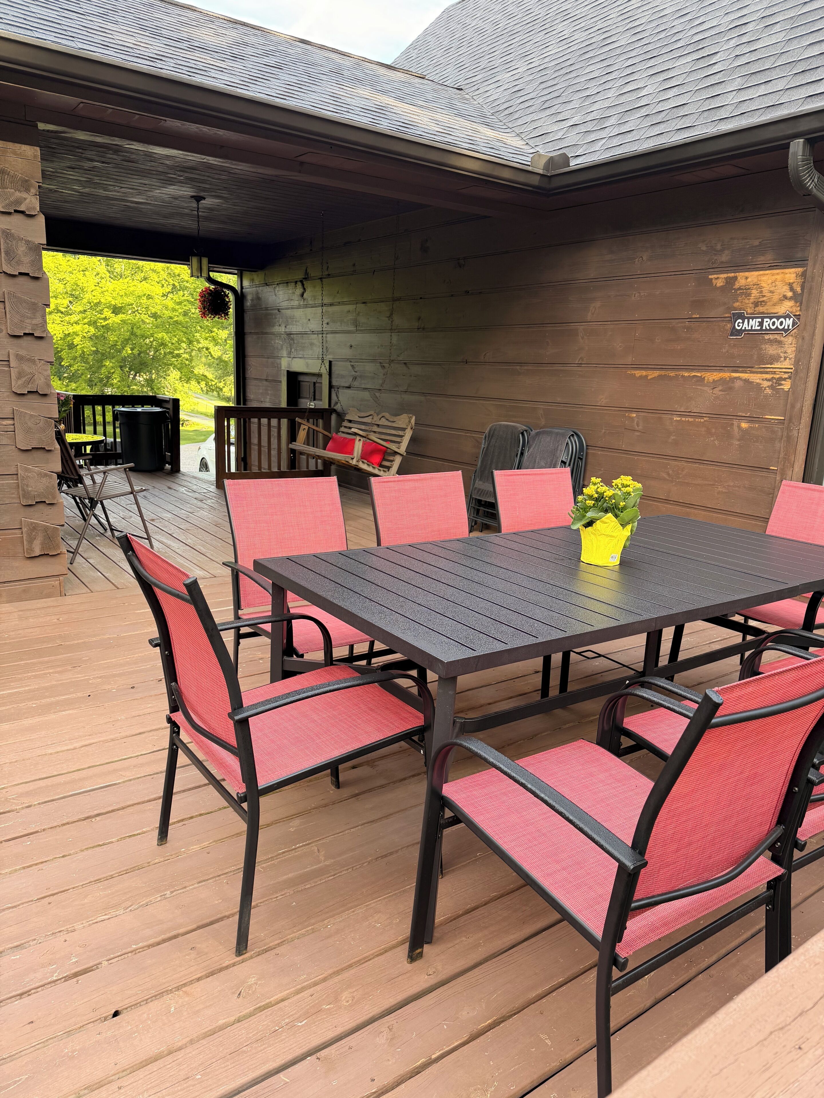 An outdoor patio with a table and chairs, a sign indicating a game room, and a view of greenery.
