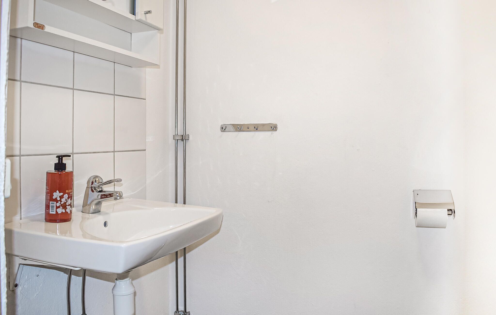 A bathroom with a white sink, a faucet, a bottle of hand soap, and a towel dispenser.