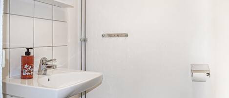 A bathroom with a white sink, a faucet, a bottle of hand soap, and a towel dispenser.