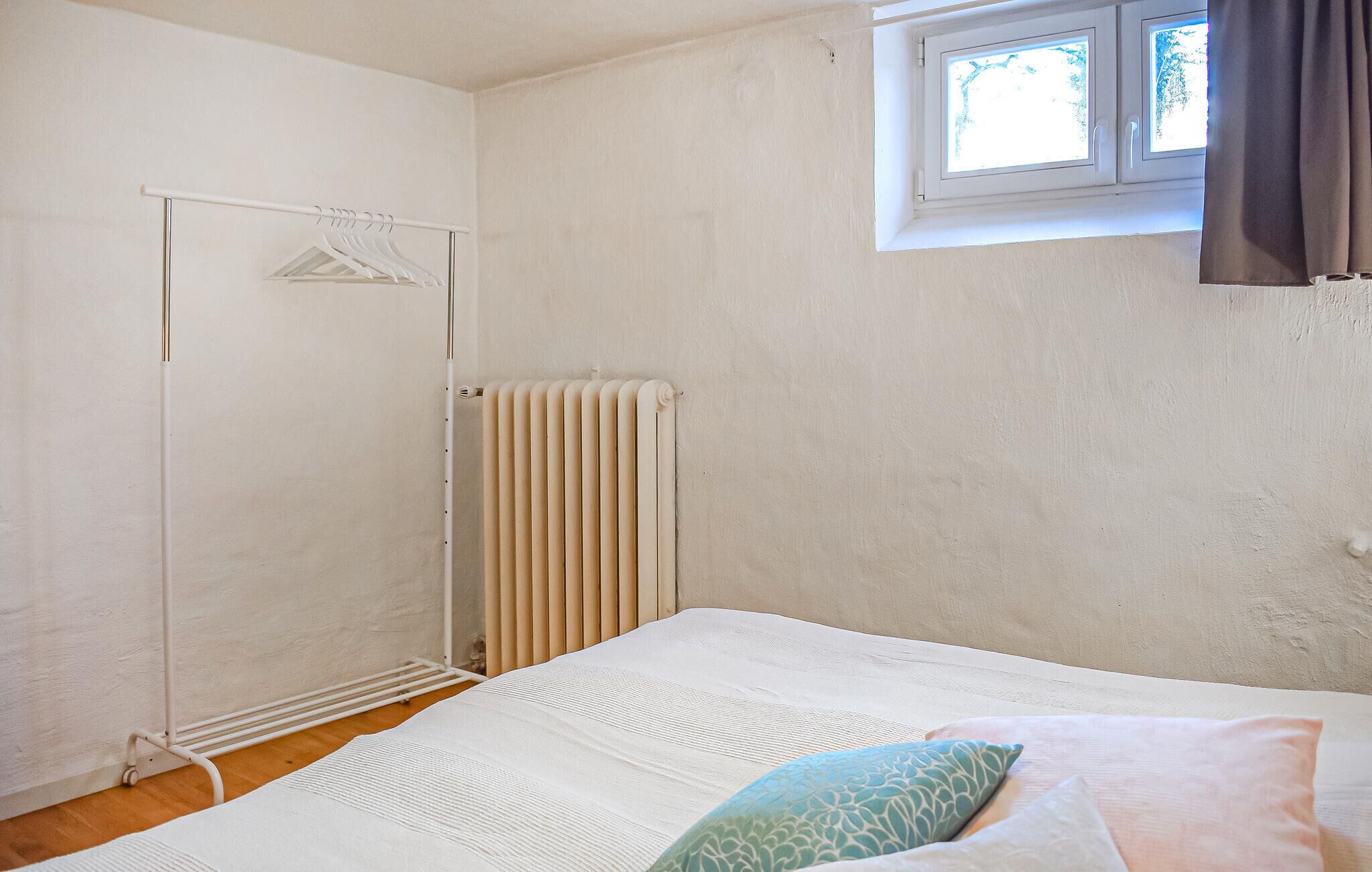 A bedroom with a bed, a radiator, a window with curtains, and a clothes drying rack.