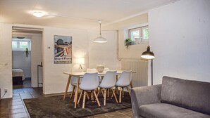 Una sala de estar con un sofá gris, una mesa de comedor con sillas, una alfombra y un cartel en la pared.