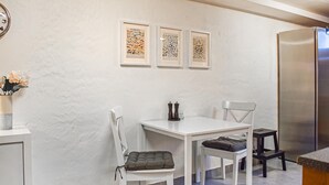 Una cocina con una mesa blanca, dos sillas, un refrigerador y tres cuadros en la pared.