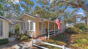 Een geel huis met een veranda, een witte hek en een Amerikaanse vlag.
