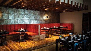 A restaurant with wooden floors, red cushioned seating, and a stone wall. Tables are set with plates and glasses. - Fiji -Wyndham- Beachfront Resort- Denarau - 3 BR (Nadi)