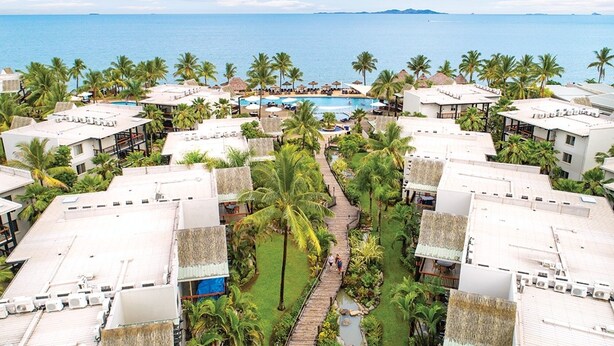 A resort with multiple buildings, a central pool, and palm trees.