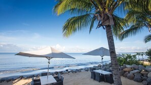 A beachside seating area with tables and umbrellas, overlooking the ocean.