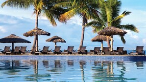 A poolside area with lounge chairs and thatched umbrellas, surrounded by palm trees.