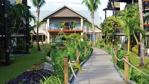 A resort with a central building, a wooden pathway, and tropical landscaping.