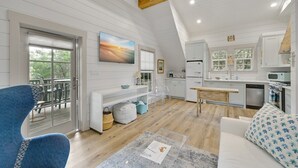 Amplia sala de estar con techo de madera, cocina con armarios blancos y comedor con banco.