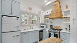 Una cocina con armarios blancos, una mesa de madera, una estufa, un microondas y un fregadero.
