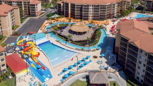 Ein Resort mit großem Pool, Wasserrutschen und Strandbereich mit Sonnenschirmen.