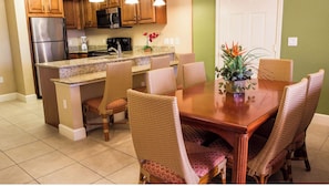 A kitchen with a built-in island, stainless steel refrigerator, microwave, and stove. There is a dining table with wicker chairs and a potted plant. - Luxury 1BR Villa Deluxe Suite - Kitchen, A/C, pool. Minutes from all attractions (Orlando)