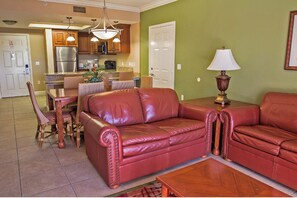 A living room with a red leather sofa, a wooden coffee table, and a dining area with wicker chairs. - Luxury 1BR Villa Deluxe Suite - Kitchen, A/C, pool. Minutes from all attractions (Orlando)