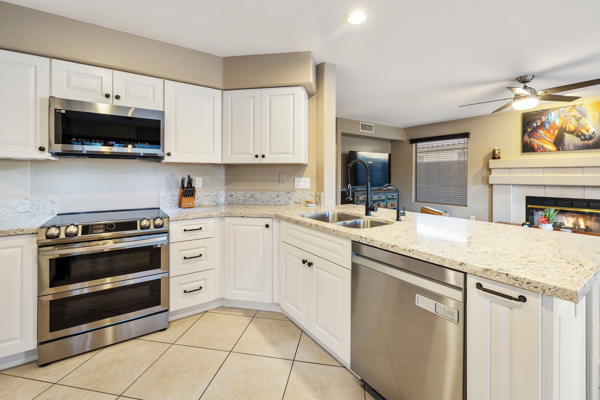 A modern kitchen with white cabinets, stainless steel appliances, a granite countertop, and a ceiling fan.