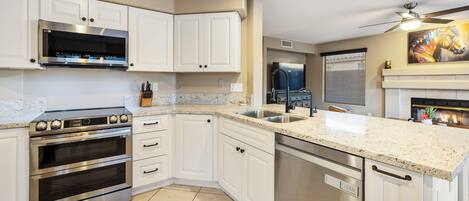 A modern kitchen with white cabinets, stainless steel appliances, a granite countertop, and a ceiling fan.