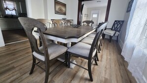 Un coin repas avec une table et des chaises en bois, un tableau au mur et une vue sur la cuisine.