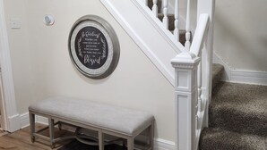 Un escalier avec des balustrades blanches et une main courante en bois, un banc au bas de l’escalier et un panneau circulaire fixé au mur.