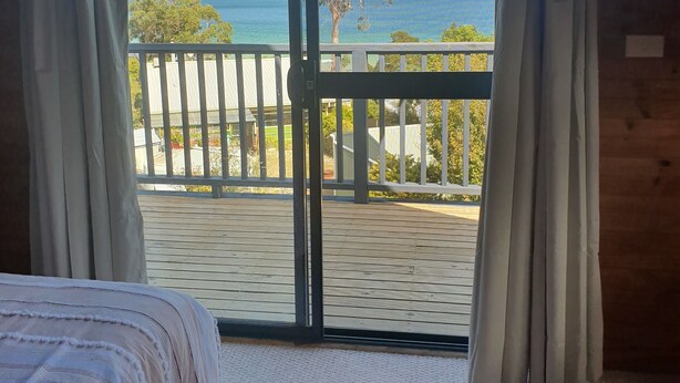 Een slaapkamer met een grote schuifdeur die leidt naar een balkon met uitzicht op zee en bomen.
