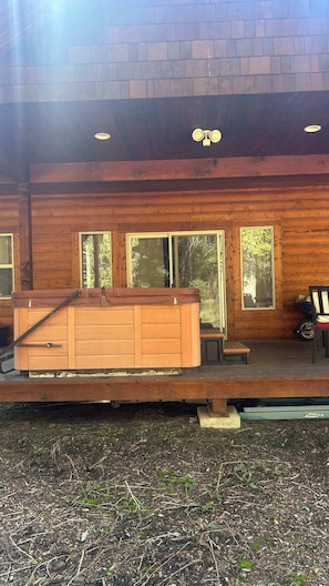 Une cabane en bois dotée d’un bain à remous, de grandes fenêtres et d’une terrasse.