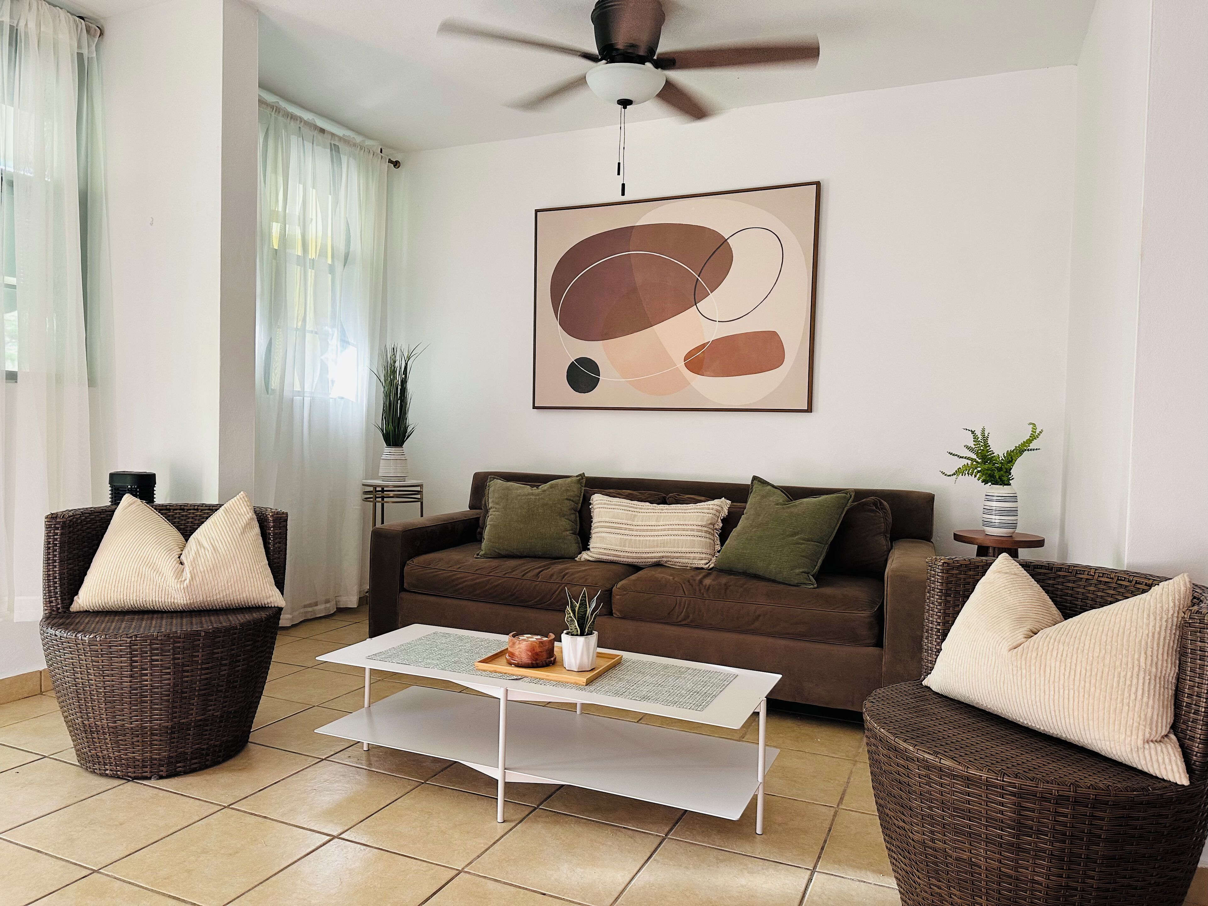 A living room with a brown sofa, two wicker chairs, a white coffee table, and a ceiling fan.