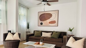 A living room with a brown sofa, two wicker chairs, a white coffee table, and a ceiling fan.