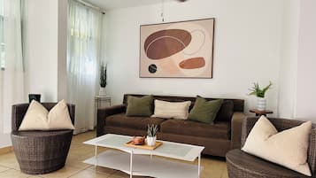A living room with a brown sofa, two wicker chairs, a white coffee table, and a ceiling fan.