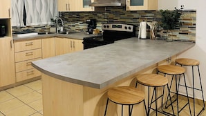 A modern kitchen with a central island, wooden cabinets, a stainless steel range hood, and a tiled backsplash.