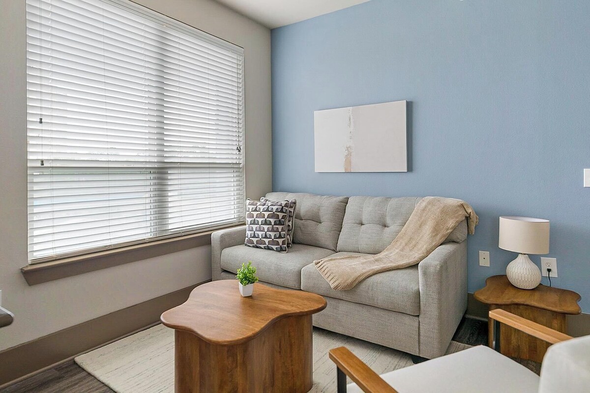 Uma sala de estar com um sofá, uma mesa de centro, um abajur e um quadro na parede.