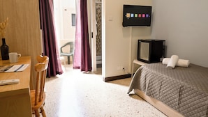 Ein Hotelzimmer mit Bett, Fernseher, Schreibtisch mit Stuhl und einem Fenster mit Vorhängen.