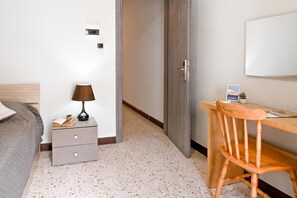 A hotel room with a bed, bedside table, lamp, desk, chair, and a door. - Sea Breeze Bay Guesthouse - B5, Saint Paul's Bay, Malta (Saint Paul's Bay)
