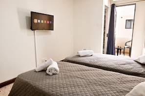 A hotel room with two beds, a TV mounted on the wall, and a bathroom visible through an open door.