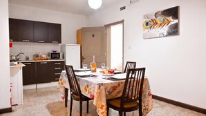 A dining area with a table set for four, kitchen cabinets, a refrigerator, and a door leading to another room. - Sunny Ensuite by the Sea - B4, Saint Paul's Bay, Malta (Saint Paul's Bay)