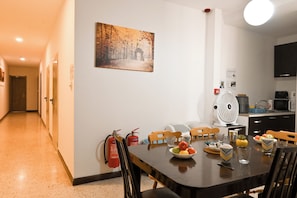 A dining area with a table set for two, a fire extinguisher mounted on the wall, and a kitchen area with a microwave and a fan. - Sea Breeze Bay Guesthouse - B4, Saint Paul's Bay, Malta (Saint Paul's Bay)