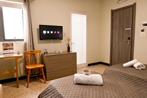 Ein Hotelzimmer mit einem Bett, einem Schreibtisch mit Stuhl, einem Fernseher und einer Tür.