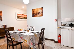 En matplats med ett bord dukat för två personer, ett kök med en spis och kastruller, och två inramade tavlor på väggen.