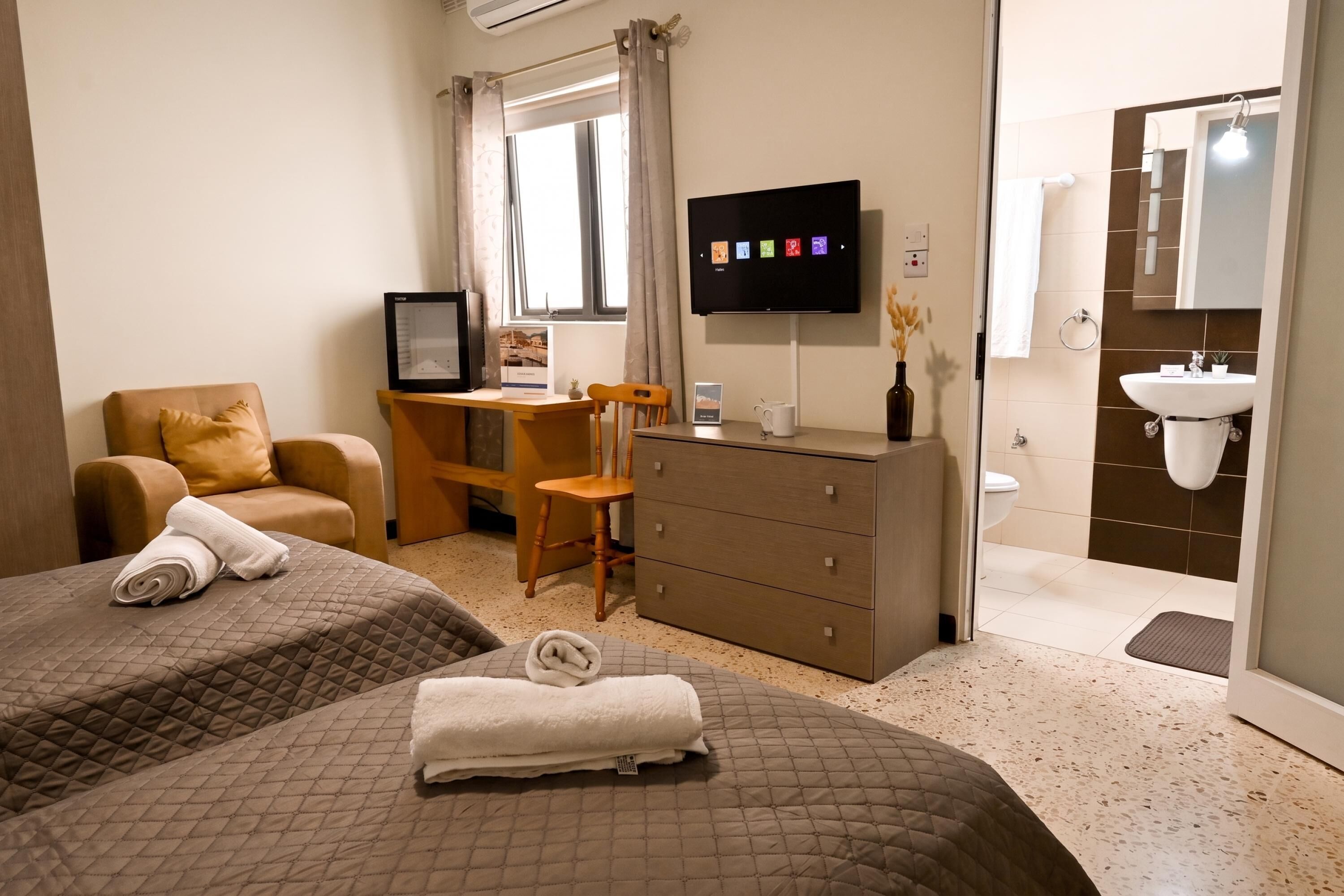 A hotel room with two beds, a desk, a TV, a dresser, and a bathroom.